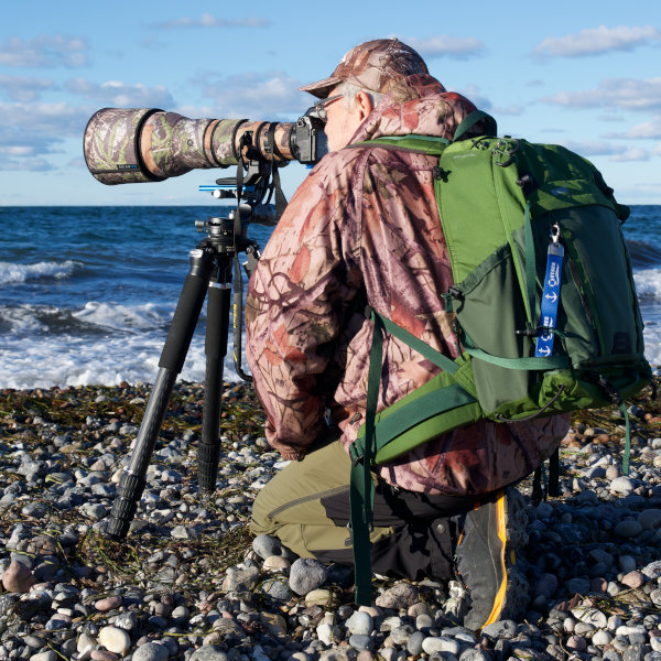 Naturfotograf mit Teleobjektiv und Stativ bei der Vogelbeobachtung an der Ostseeküste.